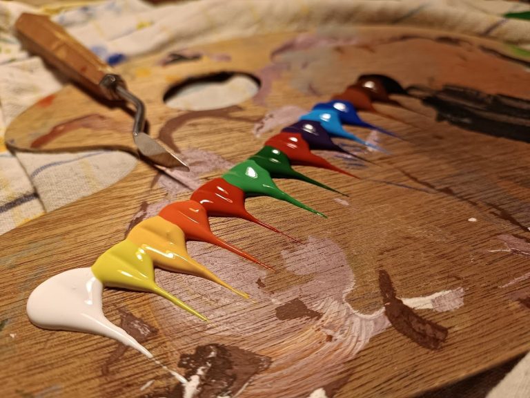 Farben auf einer Holzpalette in Regenbogenfarben, bereit zum Malen.